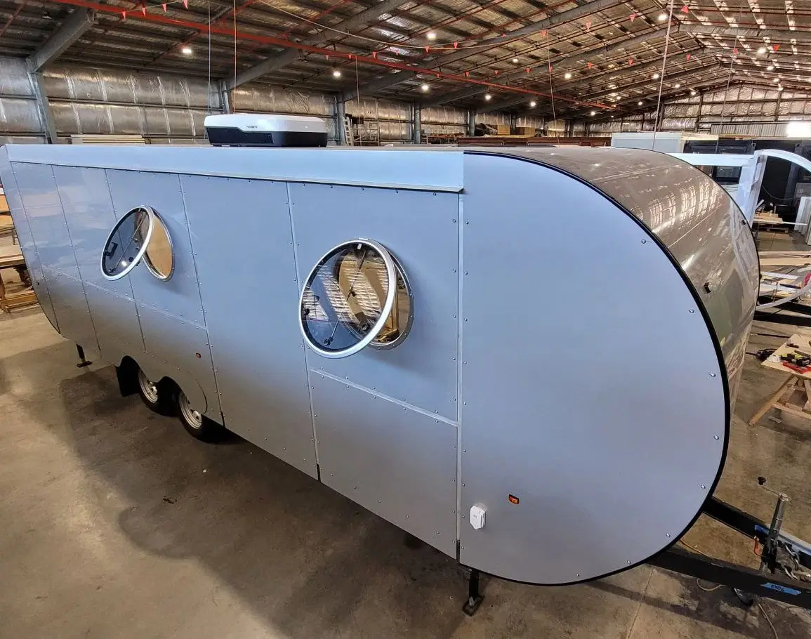 Two opening porthole windows on the side of a caravan, showcasing the design and functionality with screens visible.